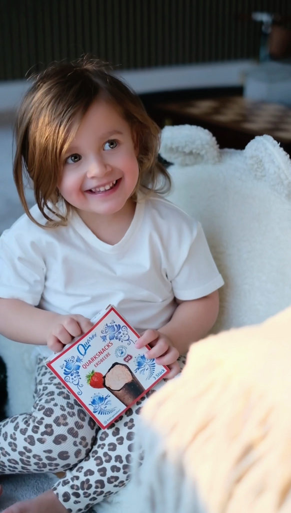 Lachendes Mädchen hält eine Packung Quarki Quarksnacks Erdbeere
