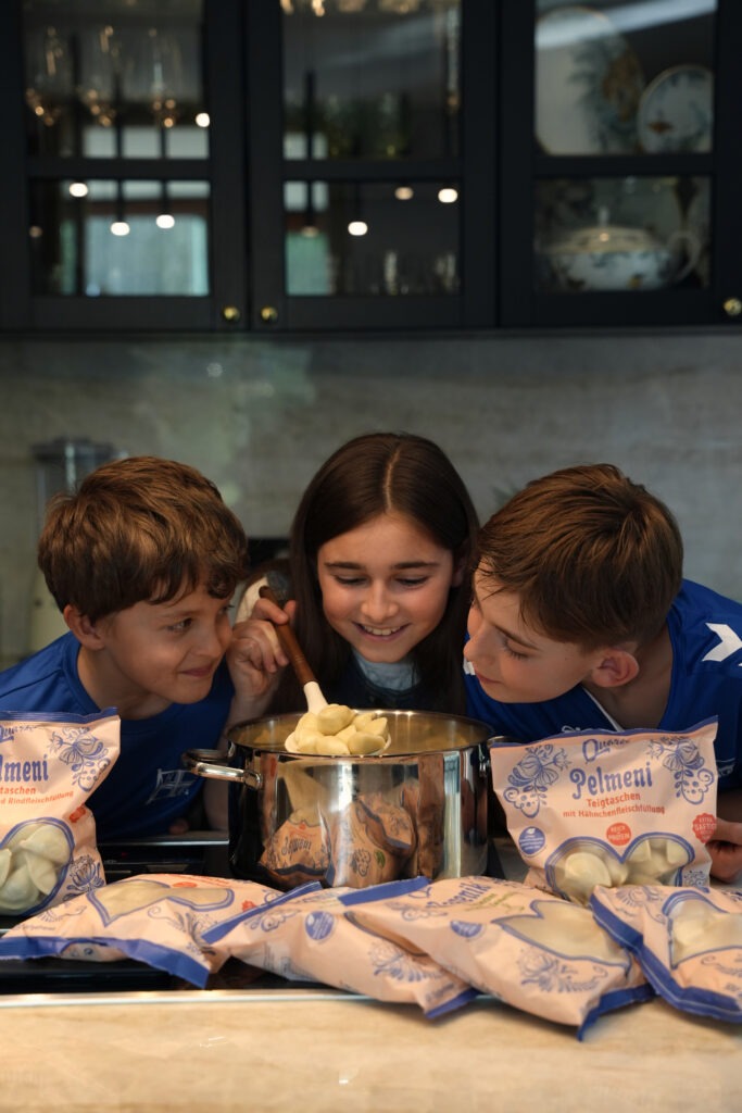Drei Kinder rühren gemeinsam Pelmeni von Quarki im Topf